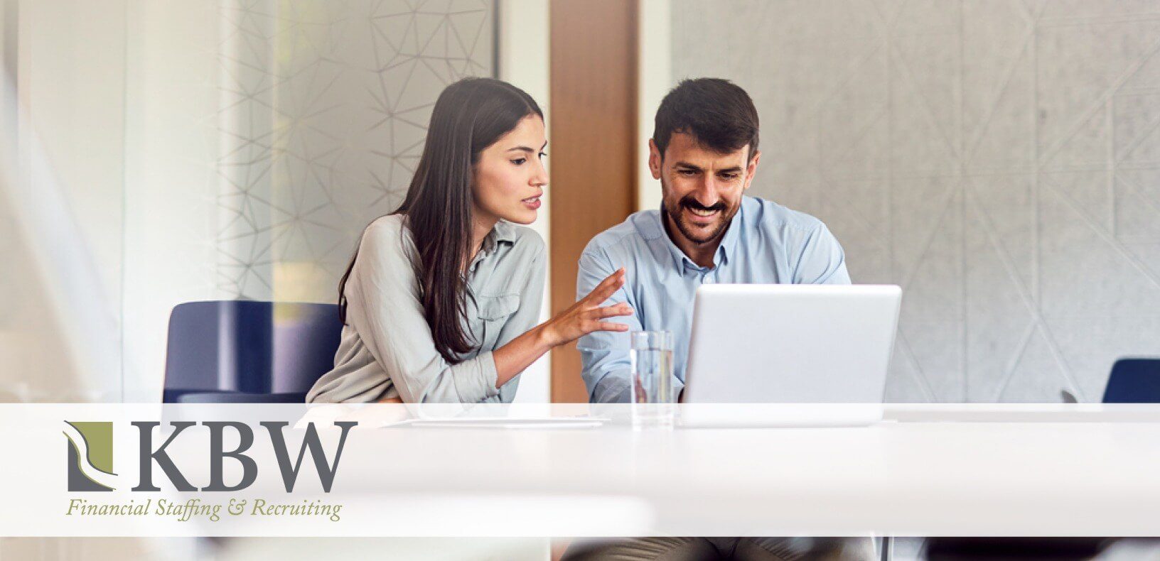 A man and woman sitting at a table looking at a computer and talking