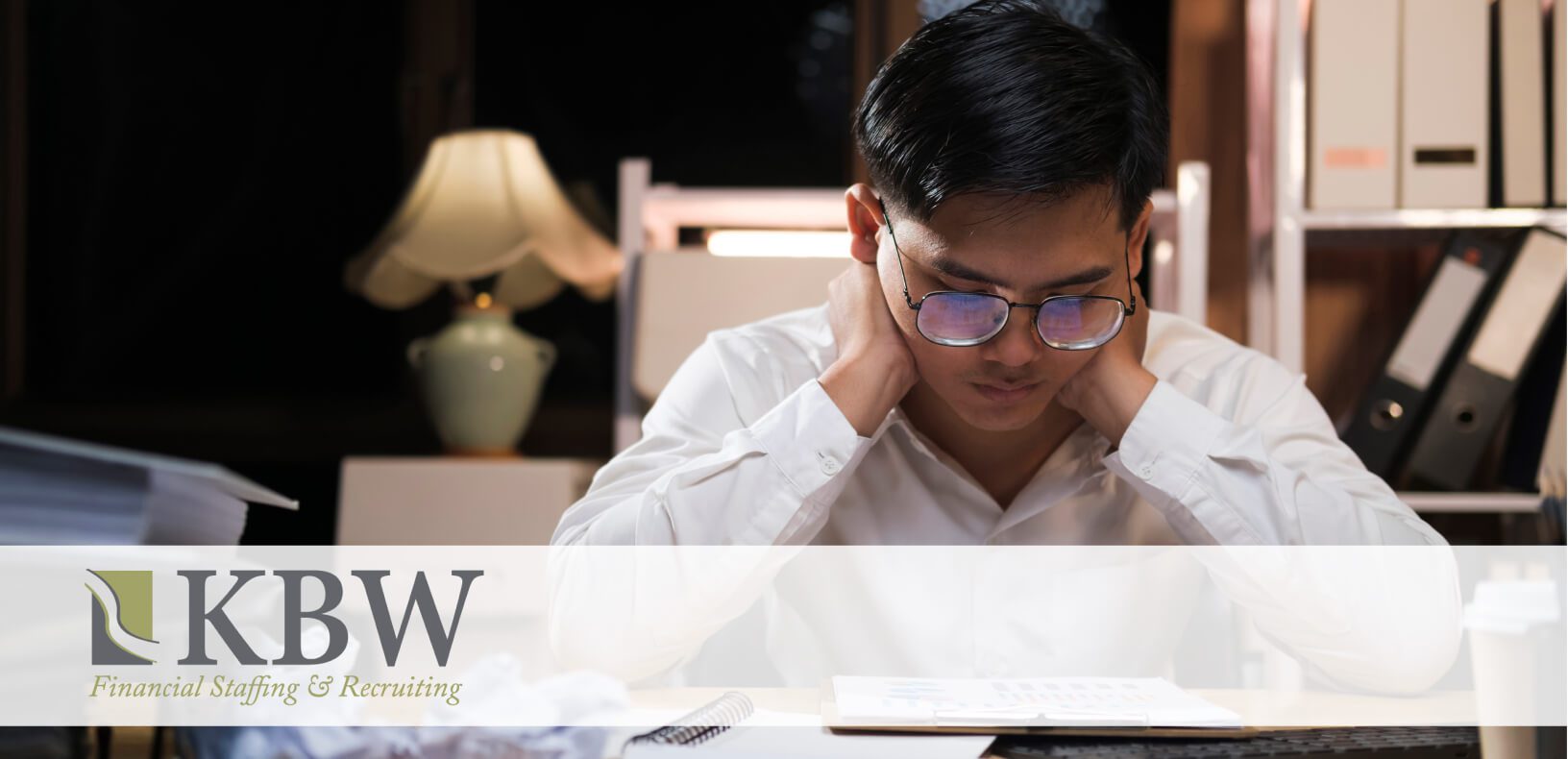 A man sitting at a desk with his head resting on his hands looking at a document